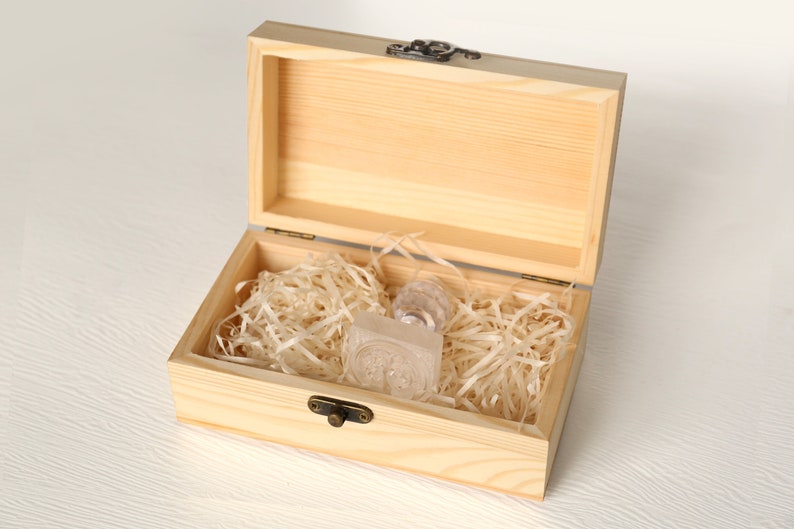 May include: A wooden box with a hinged lid, open to reveal a clear glass stamp inside. The box is filled with shredded paper for cushioning.