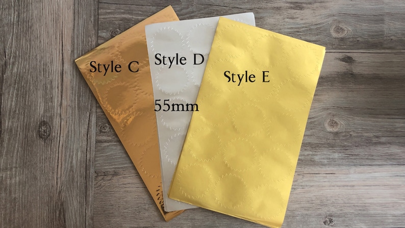 以下が含まれることがあります： 金、白、黄色の異なるデザインのステッカー用紙3枚。シートには「Style C」、「Style D」、「Style E」とラベル付けされています。白いシートには「55mm」の文字が印刷されています。