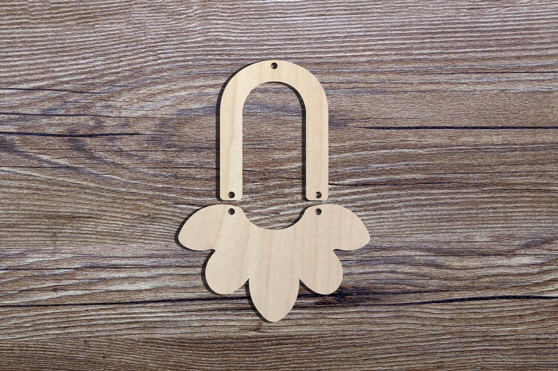 May include: Unfinished wooden earring components. The set includes an arched top piece and a floral-shaped bottom piece, each with pre-drilled holes for assembly. The natural wood grain is visible against a brown wood background.