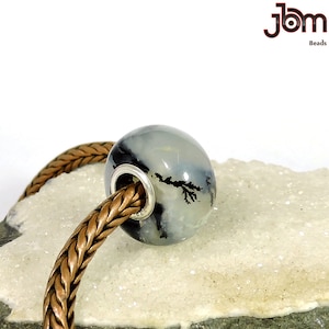 May include: A white and black agate bead with a dendritic pattern. The bead is on a copper chain.