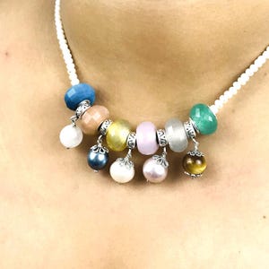 Op de afbeelding: Een kleurrijke ketting met een witte kralenketting, met diverse edelsteen kralen en hangende bedels. De kralen hebben blauwe, perzik, gele, roze en groene tinten. Bedels zijn onder meer parels en een tijgeroog kraal.