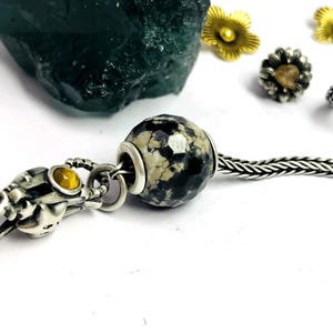 May include: A white ceramic mug with a black handle and the text "But First, Coffee" in a bold, black font. The mug is set against a blurred background, suggesting a cosy setting.