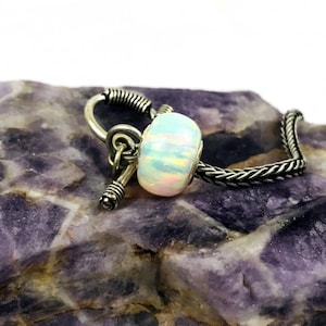 May include: A silver charm bracelet with a white opal bead and a silver toggle clasp.