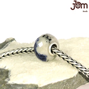K&ouml;nnte beinhalten: Eine facettierte Perle mit einem hellgrauen und blauen Muster, auf einer silbernen Kette aufgef&auml;delt. Die Perle hat einen silberfarbenen Metallkern. Das Bild enth&auml;lt den Text "JBM Beads".