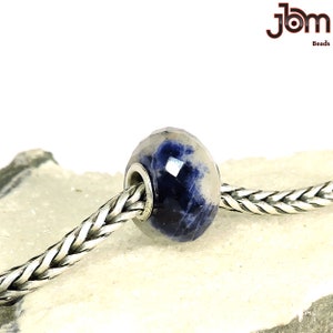 K&ouml;nnte beinhalten: Eine facettierte Perle mit blau-wei&szlig;em Muster, auf einer silbernen Kette aufgef&auml;delt. Die Perle hat einen Kern aus silberfarbenem Metall. Das Bild enth&auml;lt den Text "jbm Beads" in der oberen rechten Ecke.