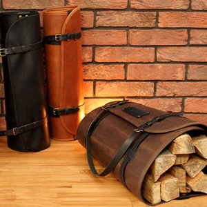 May include: Three leather firewood carriers. Two are rolled up and have straps and buckles. The third is unrolled and filled with firewood logs. The carriers are brown, black, and tan.