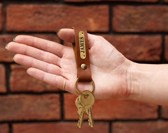 May include: Brown leather keychain with a brass key ring and two keys. The keychain has a brass tag with the name "JAMES" engraved on it.