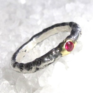 Puede incluir: Un anillo de plata con un acabado texturizado y una sola piedra preciosa roja engastada en un engaste de oro.