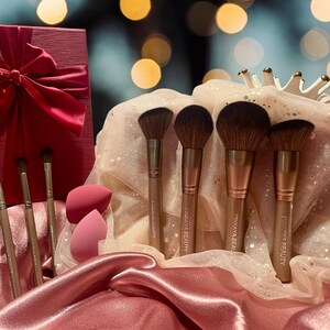 May include: A set of six makeup brushes with rose gold handles and soft bristles. The brushes are arranged in a pink and white tulle bag with two pink makeup sponges. The brushes are labeled "Pinkaya Beauty".