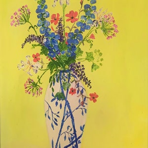 Puede incluir: Una pintura de naturaleza muerta de un arreglo floral en un jarrón blanco con detalles azules estilo bambú. El ramo incluye flores azules, rojas y blancas sobre un fondo amarillo. Una mesa rosa con un borde decorativo está en primer plano.