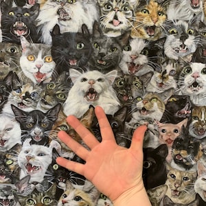 May include: A fabric pattern featuring a multitude of cat faces with open mouths and various expressions. The cats are in shades of gray, black, white, and brown. The image includes a hand for scale.