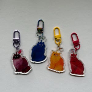 May include: Four acrylic keychains featuring fluffy creatures with wide eyes and antennae. The creatures are purple, dark blue, orange, and red, each attached to a matching colored metal lobster clasp, with the blue one on a rainbow-toned clasp.
