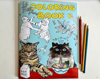 May include: A colouring book titled "COLORING BOOK II" featuring cat illustrations, including cats fighting, eating ramen, and drinking milk. The book is accompanied by three coloured pencils: red, yellow, and blue.