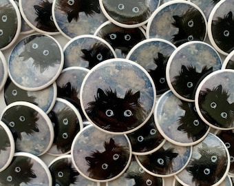 May include: A collection of round, white-rimmed buttons with a black cat illustration on each. The cats have large, blue eyes and are set against a blue and white watercolor background.