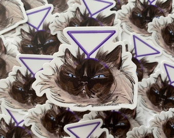 May include: A close-up of a sticker featuring a cartoon illustration of a fluffy brown cat with blue eyes. The cat is wearing a purple triangle above its head. The sticker has the text "@rebeccasalinasart" at the bottom.
