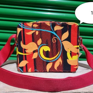 May include: A red crossbody bag with a black, orange and yellow floral pattern. The bag has a red adjustable strap.