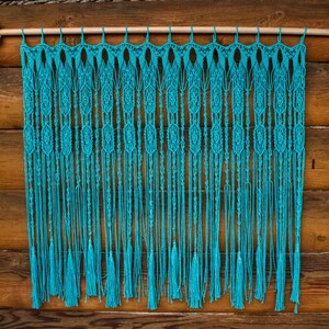 May include: A turquoise macrame wall hanging with a wooden dowel rod at the top. The macrame has a fringe at the bottom and is made with a knot pattern.