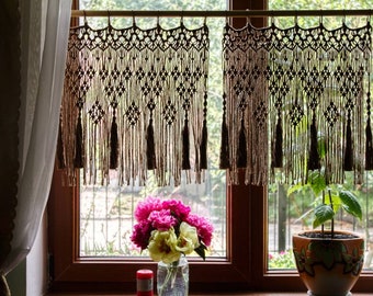 May include: Two macrame curtains with tassels hang in a window with a bouquet of pink and white peonies in a glass vase on the windowsill.