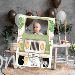 May include: A green jeep photo booth prop with a cut-out for a face. The jeep has a "Louie's 1st Birthday!" sign on the front. There are animal illustrations around the jeep, including a lion, elephant, and zebra.