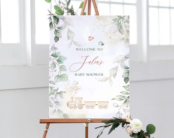 May include: A white welcome sign with green foliage and gold accents. The sign says "Welcome to Julia's Baby Shower" and features a cartoon train with balloons.