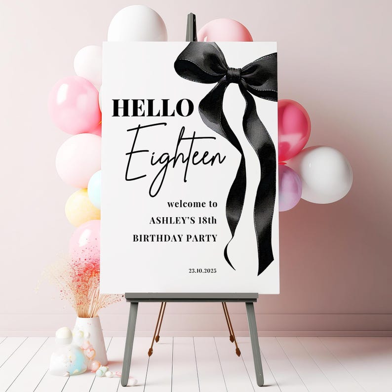 May include: A white welcome sign with black text and a black satin ribbon bow. The text reads "HELLO Eighteen welcome to ASHLEY'S 18th BIRTHDAY PARTY 23.10.2023".