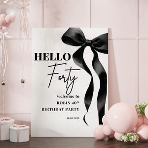 May include: A white sign with black text and a black bow. The text reads "HELLO Forty welcome to ROBIN 40th BIRTHDAY PARTY 18.09.2025".