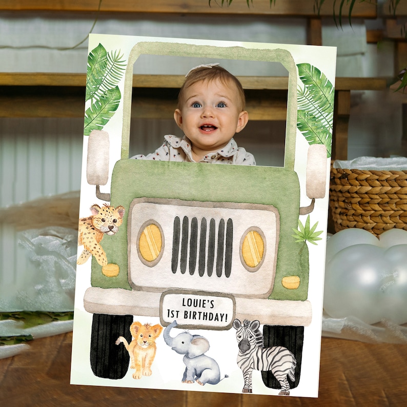 May include: A green jeep photo booth prop with a cut-out for a face. The jeep has a number plate that says "Louie's 1st Birthday!" and is surrounded by jungle animals including a lion, elephant, and zebra.