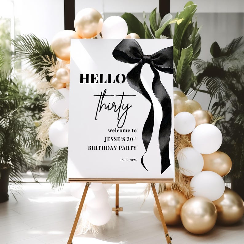 May include: A white welcome sign with black text and a black satin ribbon bow. The text reads "HELLO thirty welcome to JESSE'S 30th BIRTHDAY PARTY 18.09.2025".