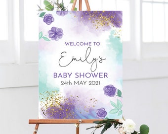 May include: Welcome to Emily's Baby Shower sign with a watercolor background in shades of purple, blue, and green. The sign features gold glitter accents and purple flowers.