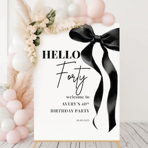 May include: A white sign with black text and a black ribbon bow. The text reads "HELLO Forty" and "welcome to AVERY'S 40th BIRTHDAY PARTY 18.09.2025".
