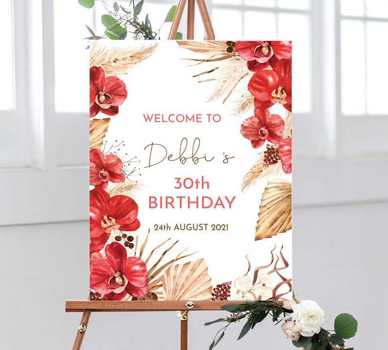 May include: Welcome to Debbi's 30th Birthday sign with a tropical theme. The sign features red orchids, dried palm leaves, and a white background. The text is in a brown font.