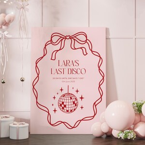 May include: A pink poster with a red outline of a ribbon bow and a disco ball. The text on the poster reads "LARA'S LAST DISCO 20 DAYS UNTIL SHE SAYS 'I DO' 13th June 2025".