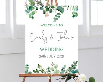 Op de afbeelding: Een wit huwelijksbord met een groene bladrand. Het bord staat er: "Welkom bij Emily & John's Wedding 24 juli 2021".