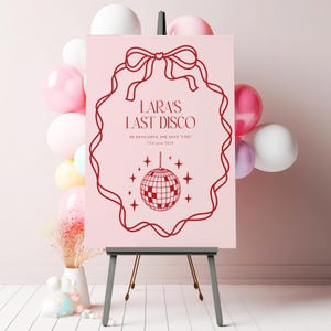 May include: A pink sign with a red border and a red bow at the top. The sign says "Lara's Last Disco" and "20 days until she says "I do" 13th June 2023". A red disco ball with stars is in the center of the sign.