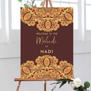 May include: A brown welcome sign with gold ornate designs and the text "Welcome to the Mehndi of Hadi".