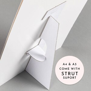 May include: White cardboard stand with a fold-out support. The stand is designed to hold a poster or print. The text on the stand reads "A4 & A3 COME WITH STRUT SUPORT".