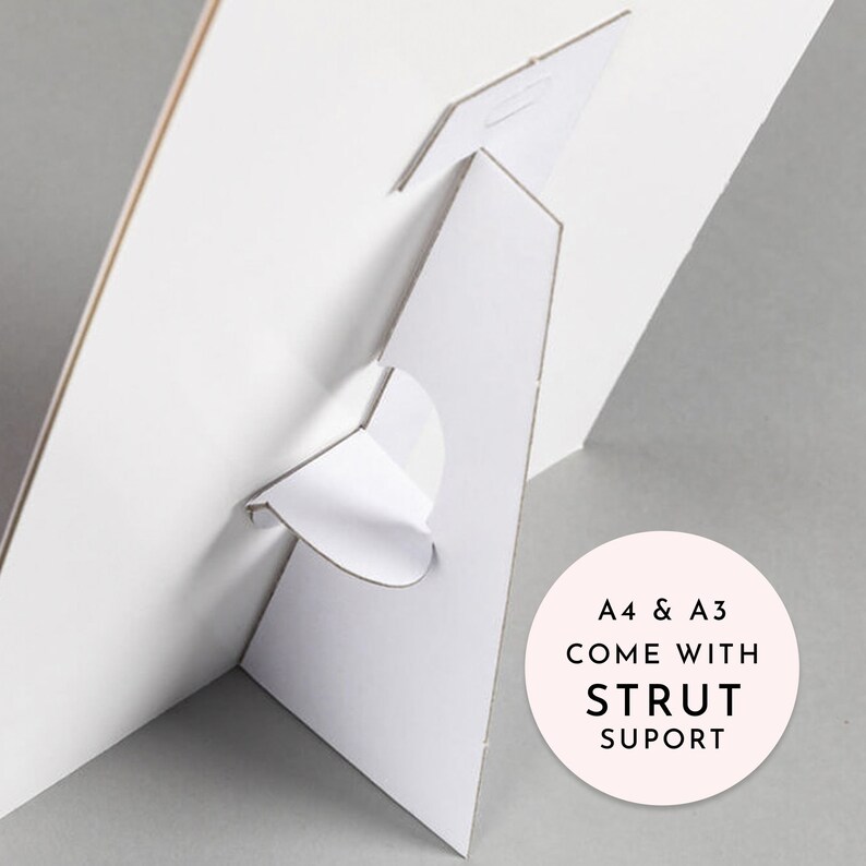 May include: White cardboard stand with a fold-out support. The stand is designed to hold a poster or print. The text on the stand reads "A4 & A3 COME WITH STRUT SUPORT".