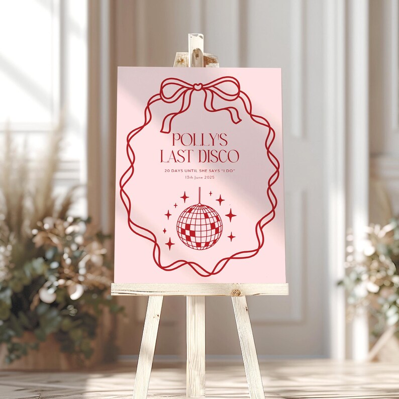 May include: A pink sign with a red border and a red bow at the top. The sign says "Polly's Last Disco" and "20 days until she says 'I do'" with the date "13th June 2023". A red disco ball is in the center of the sign.