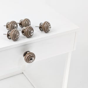 Peut inclure: Ensemble de sept boutons de cabinet en céramique brune avec des motifs en spirale blancs et des accents argentés. Les boutons sont présentés sur une surface blanche.