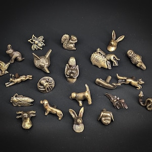 Peut inclure: Une collection de petites figurines d'animaux de couleur bronze, dont un lapin, un écureuil, un renard, une abeille, un chien et un hibou. Les figurines sont finement détaillées et disposées sur une surface sombre, présentant une variété d'animaux sauvages.