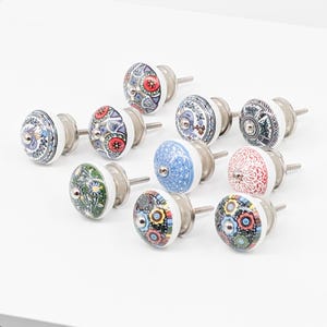 Op de afbeelding: Assortiment van tien keramische kastknoppen met kleurrijke bloem- en geometrische patronen. Elke knop heeft een zilveren metalen schroef.