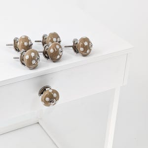 May include: Six brown ceramic cabinet knobs with white polka dots. The knobs are shown on a white surface.