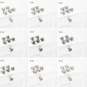 Könnte beinhalten: Neun Sätze Keramik-Schubladengriffe mit verschiedenen Mustern. Jedes Set enthält vier Griffe mit silberner Oberfläche. Die Griffe sind in Reihen auf einer weißen Oberfläche angeordnet.