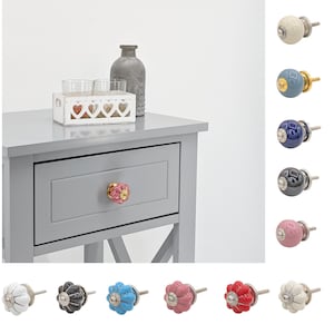 Puede incluir: Surtido de pomos de cajón de cerámica en varios colores, incluyendo blanco, azul, rosa, negro y rojo. Los pomos tienen un diseño floral y un acento dorado. Los pomos se muestran en una mesita de noche gris con un cajón.