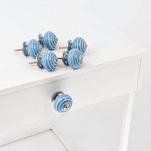 Può includere: Sei pomelli per armadi in ceramica blu con un design a spirale bianco e dettagli argentati. I pomelli sono disposti su una superficie bianca.