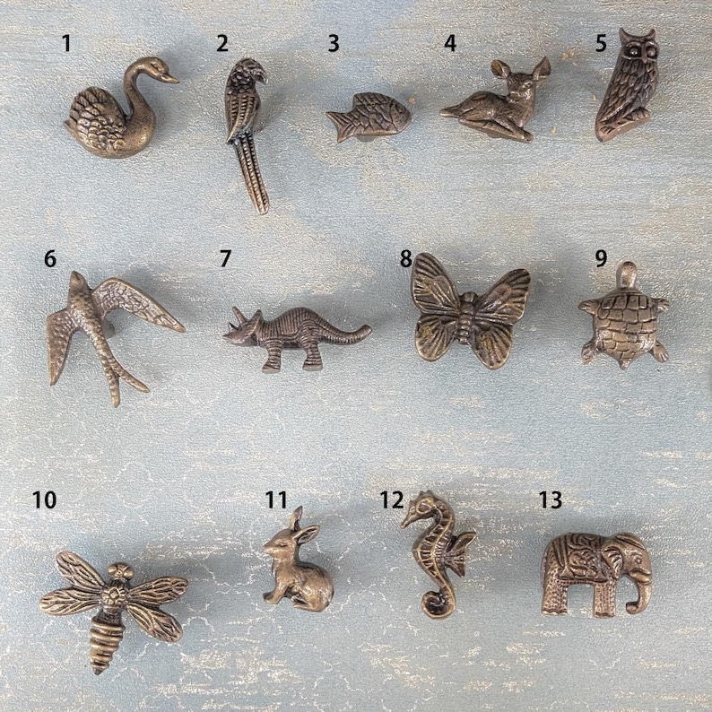 May include: A collection of bronze-toned cabinet knobs in various animal shapes, including a swan, parrot, fish, deer, owl, swallow, dinosaur, butterfly, turtle, dragonfly, rabbit, seahorse, and elephant. These decorative knobs add a unique touch to furniture.