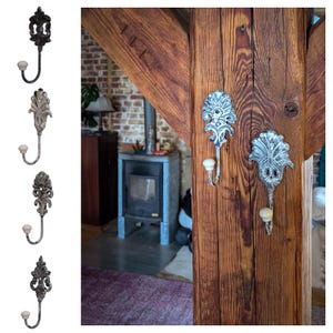 Op de afbeelding: Drie decoratieve haken met een bloemmotief in een verweerde witte afwerking. De haken zijn gemonteerd op een houten balk.