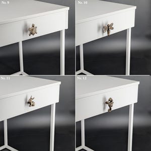 May include: Four white bedside tables with decorative drawer pulls. Each table has a different bronze-colored pull: a turtle, a bee, a rabbit, and a seahorse. The tables have a minimalist design with white legs.