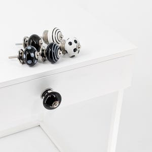 Peut inclure: Un ensemble de six boutons de tiroir en céramique noir et blanc avec des accents argentés. Les boutons ont des motifs différents, y compris des pois, des rayures et des volutes.