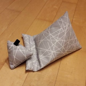 K&ouml;nnte beinhalten: Zwei graue Stoffkissen mit einem wei&szlig;en geometrischen Muster. Das kleinere Kissen ist dreieckig und das gr&ouml;&szlig;ere Kissen ist rechteckig.